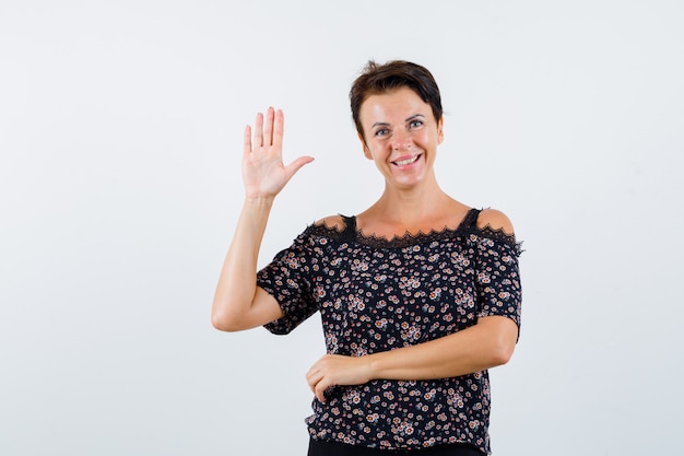 Mature woman showing stop sign in floral blouse, black skirt and looking jolly. front view.