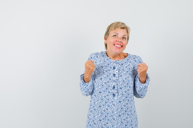 Mature woman showing success gesture in dress and looking jolly.