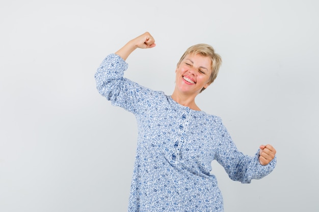 Mature woman showing winner gesture in dress and looking blissful.