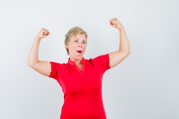 Mature woman showing winner gesture in red t-shirt and looking lucky