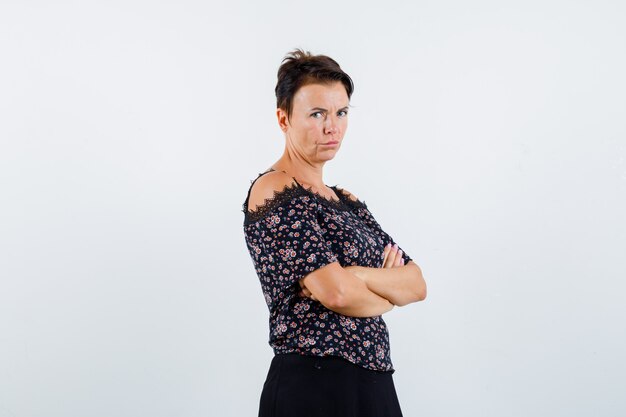 Mature woman standing arms crossed in floral blouse and black skirt and looking confident , front view.