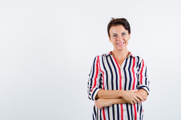 Mature woman standing arms crossed in striped shirt and looking happy. front view.
