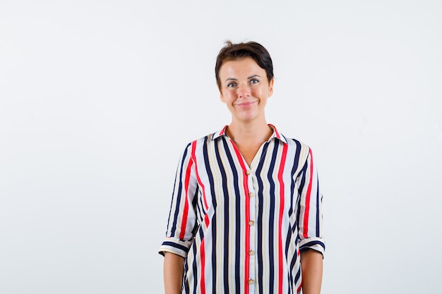 Mature woman standing straight and posing at camera in striped blouse and looking buoyant. front view.