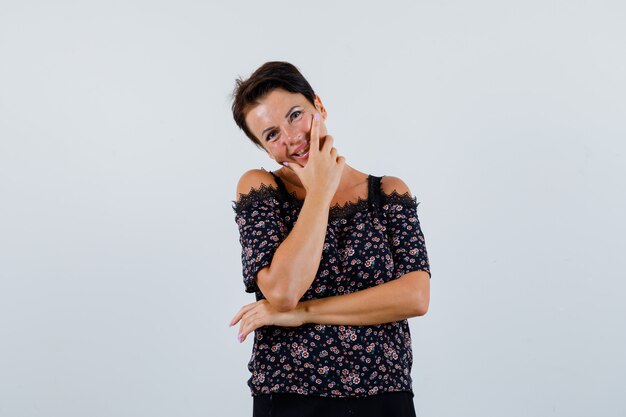 Mature woman standing in thinking pose while smiling in blouse and looking attractive , front view.