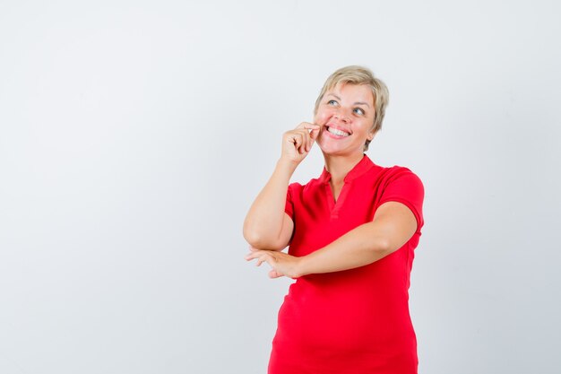 Mature woman standing while thinking in red t-shirt and looking cheerful.