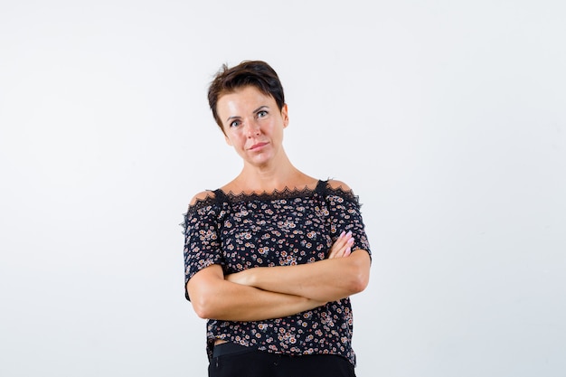 Mature woman standing with crossed arms in blouse and looking confident. front view.