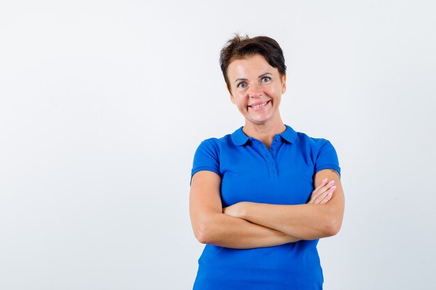 Mature woman standing with crossed arms in blue t-shirt and looking confident. front view.