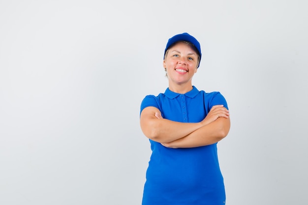 Mature woman standing with crossed arms in blue t-shirt and looking merry.