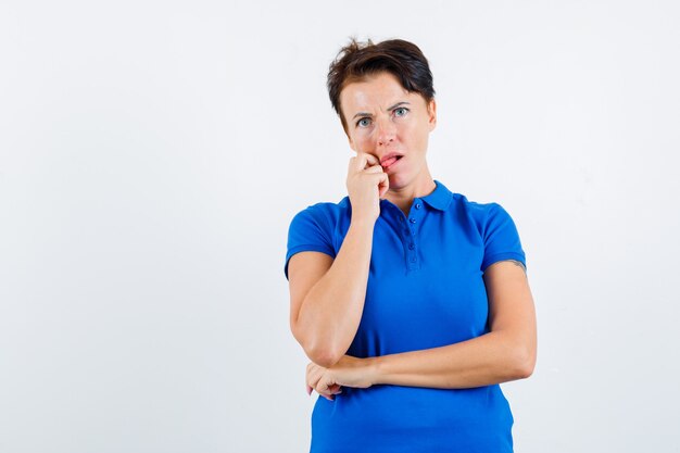 Mature woman sticking out tongue while thinking in blue t-shirt and looking puzzled. front view.