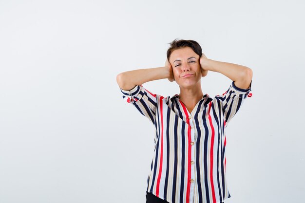 Mature woman in striped blouse holding hands on head and looking confident , front view.