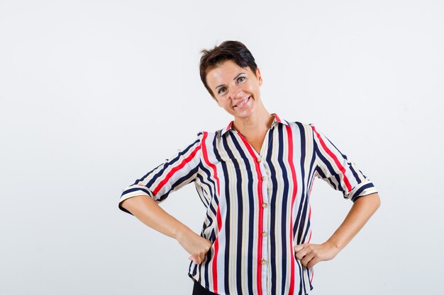 Mature woman in striped blouse holding hands on waist and looking buoyant , front view.