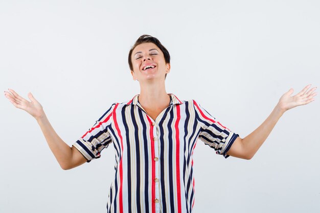 Mature woman in striped blouse showing helpless gesture and looking cheerful , front view.