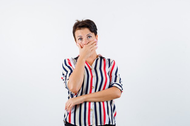 Mature woman in striped shirt covering mouth with hand and looking surprised , front view.