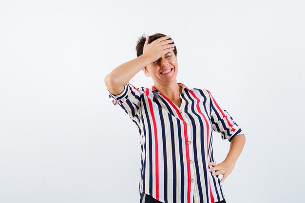 Mature woman in striped shirt holding hand on forehead and looking cheery , front view.