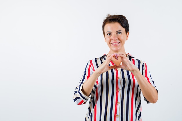 Зрелая женщина в полосатой рубашке показывает жест любви руками и выглядит счастливым, вид спереди.