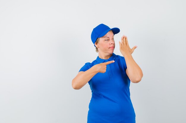 Mature woman in t-shirt pointing at her raised arm and looking focused