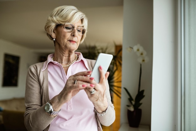Зрелая женщина пользуется мобильным телефоном и читает текстовое сообщение дома