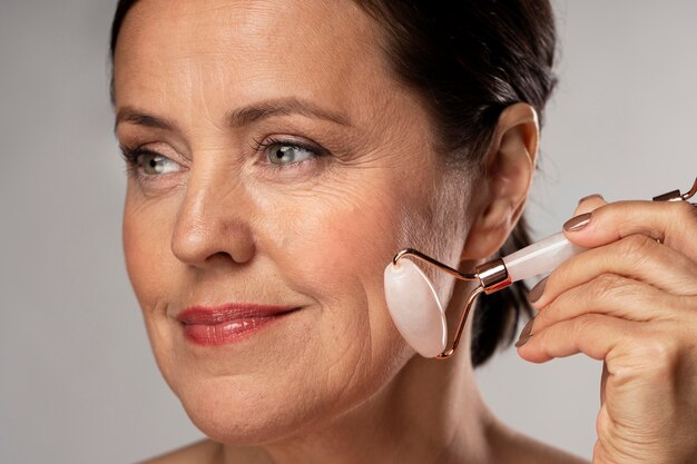 Mature woman using rose quartz face roller on her skin