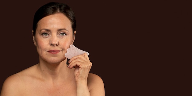 Mature woman using rose quartz face sculptor with copy space