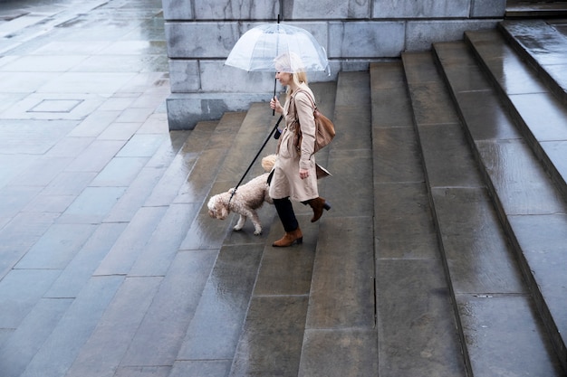 Free photo mature woman walking her dog in the city while it rains