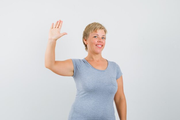 灰色のTシャツでさよならを言うために手を振って嬉しそうに見える成熟した女性