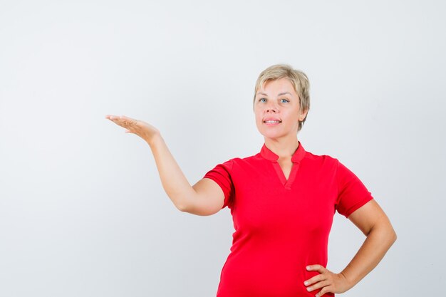 Mature woman welcoming or showing something in red t-shirt and looking confident.