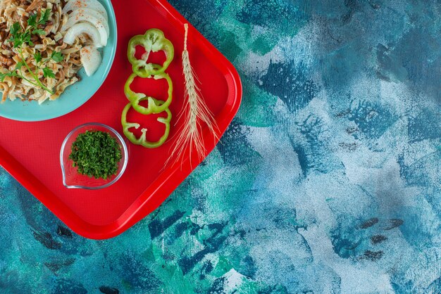 Блюда на одного с нарезанными овощами на подносе, на синем столе.