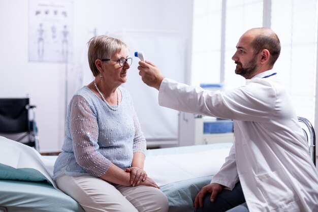 Measuring old senior woman temperature during consultation in clinic examination room