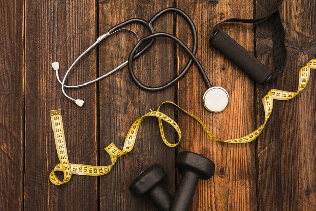 Measuring tape; dumbbell; stethoscope and fitness strap on wooden background