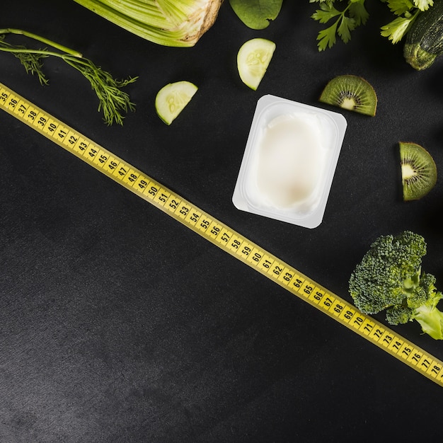 Measuring tape and various healthy green food on black backdrop