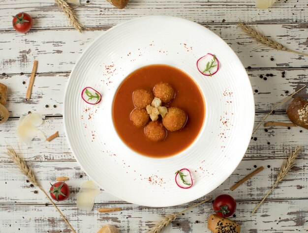 Meat ball soup in tomato sauce inside a white bowl plate.