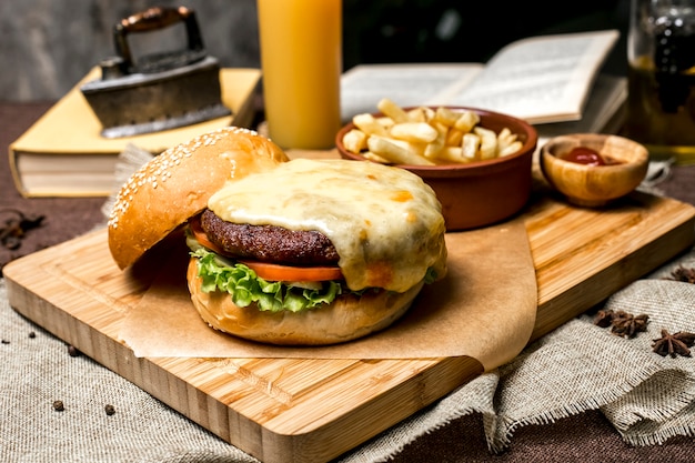 Meat burger on wooden board lettuce tomato cheese french fries ketchup side view