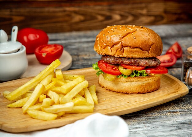 Meat burger  on wooden board  tomato  lettuce  french fries  side view