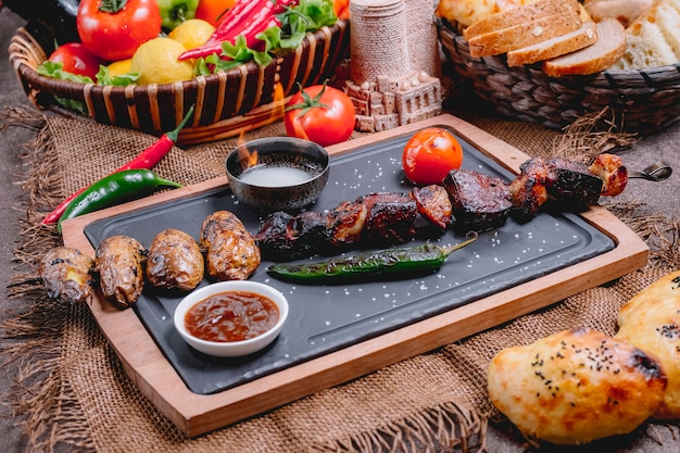 Meat kebab on wooden board potato pepper tomato adjika