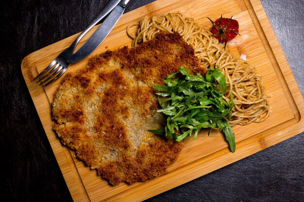 Мясо Лангет на деревянной доске с помидорами сверху спагетти рукколой
