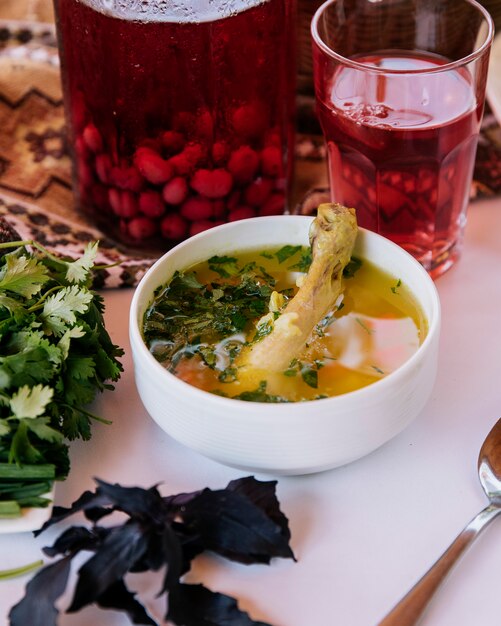 Meat piece inside broth soup with herbs and a glass of red berry composto.