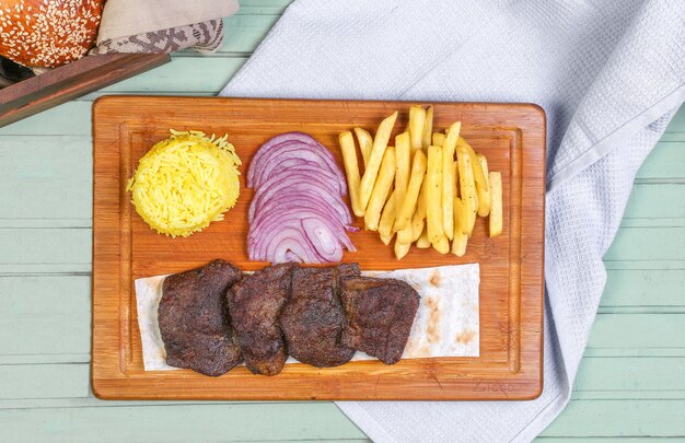 Meat steak pieces with french fries, onion and rice on the wooden board.