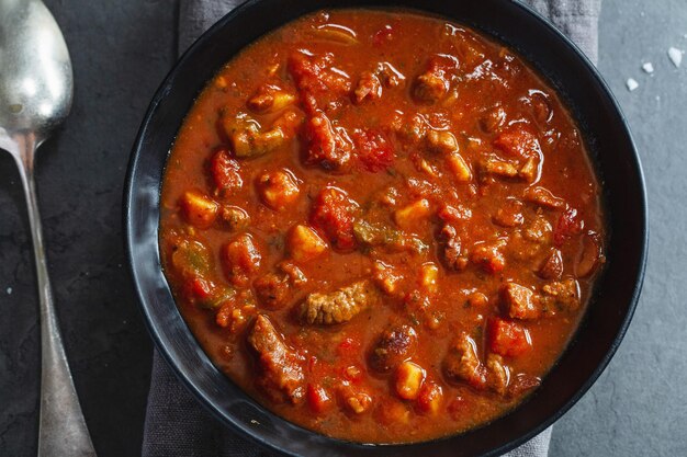 Meat and vegetable stew served in dark bowl on grey background