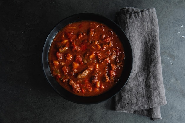 Meat and vegetable stew served in dark bowl on grey background