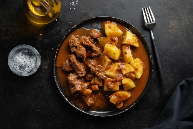 Мясо с тушеным картофелем подается на тарелке на темном фоне