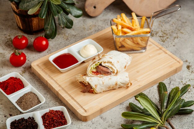 Meat wrap in flatbread served with french fries and sauces