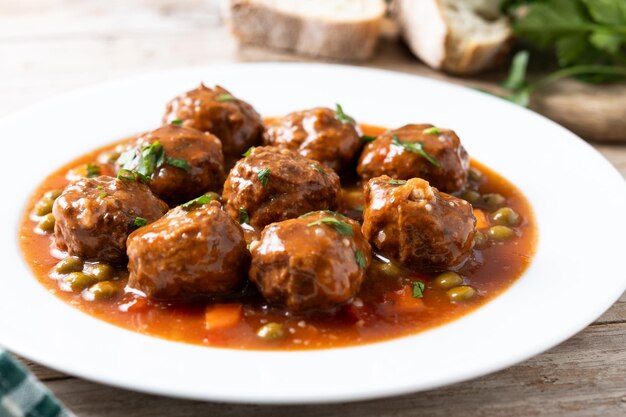 Meatballs green peas and carrot with tomato sauce on wooden table