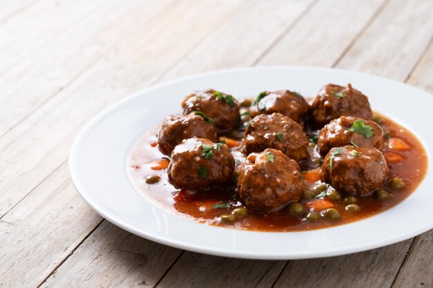 Meatballs green peas and carrot with tomato sauce on wooden table