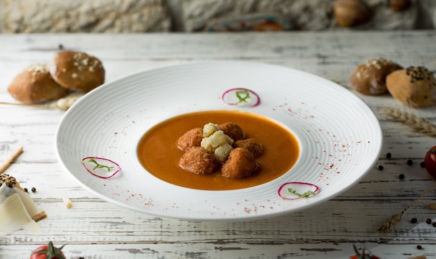 Zuppa di polpette con erbe e salsa di pomodoro all'interno del piatto bianco con focacce.