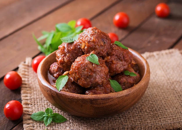 Meatballs in sweet and sour tomato sauce and basil in a wooden bowl