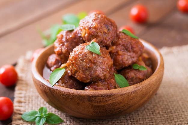 Meatballs in sweet and sour tomato sauce and basil in a wooden bowl