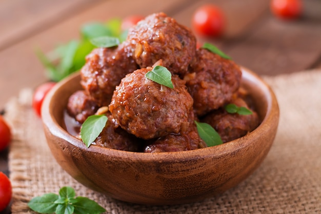 Meatballs in sweet and sour tomato sauce and basil in a wooden bowl