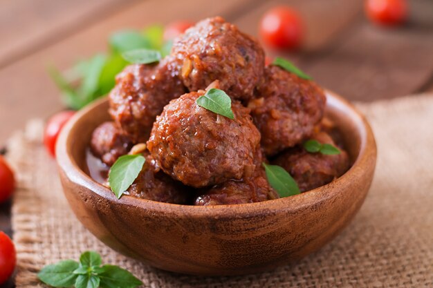 Meatballs in sweet and sour tomato sauce and basil in a wooden bowl