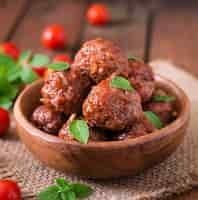 Free photo meatballs in sweet and sour tomato sauce and basil in a wooden bowl