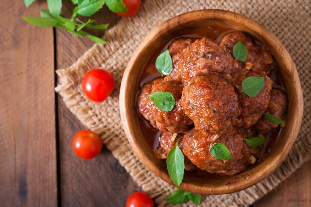 Meatballs in sweet and sour tomato sauce and basil in a wooden bowl